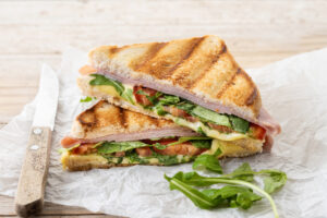 panini sandwich with ham, cheese, tomato and arugula on wooden t